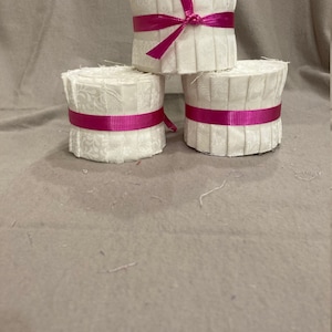 May include: Three white fabric rolls with pink ribbon tied around each roll. The rolls are stacked on top of each other.