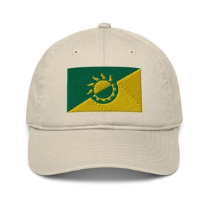 May include: A beige baseball cap with an embroidered green and yellow flag featuring a stylised sun design.