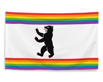 May include: A white flag with a black bear walking on its hind legs in the center. The bear has a red tongue sticking out. The flag has a rainbow stripe at the top and bottom.
