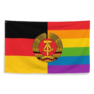 May include: A flag featuring the colours of the German flag on the left and a rainbow on the right. The German flag has a black, red, and yellow stripe. The rainbow has the colours red, orange, yellow, green, blue, indigo, and violet. In the centre of the flag is the coat of arms of the German Democratic Republic, which features a compass and hammer.