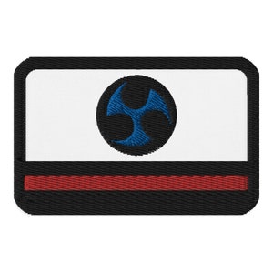 May include: Embroidered patch with a black border, white centre, and a red stripe at the bottom. A blue, stylized symbol is centred on a black circle. The patch has a rectangular shape with rounded corners.