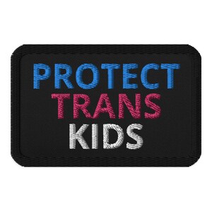Puede incluir: Parche bordado negro con el texto "PROTECT TRANS KIDS" en letras azules, rosas y blancas.