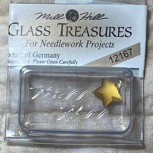 May include: A clear plastic package containing a yellow glass star. The package is labeled "Mile Hill Glass Treasures for Needlework Projects" and "12167".