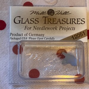 May include: A clear plastic container with a small piece of gray glass inside. The container has a label that reads "Mile Hill Glass Treasures For Needlework Projects Product of Germany Packaged USA Please Open Carefully 12051".