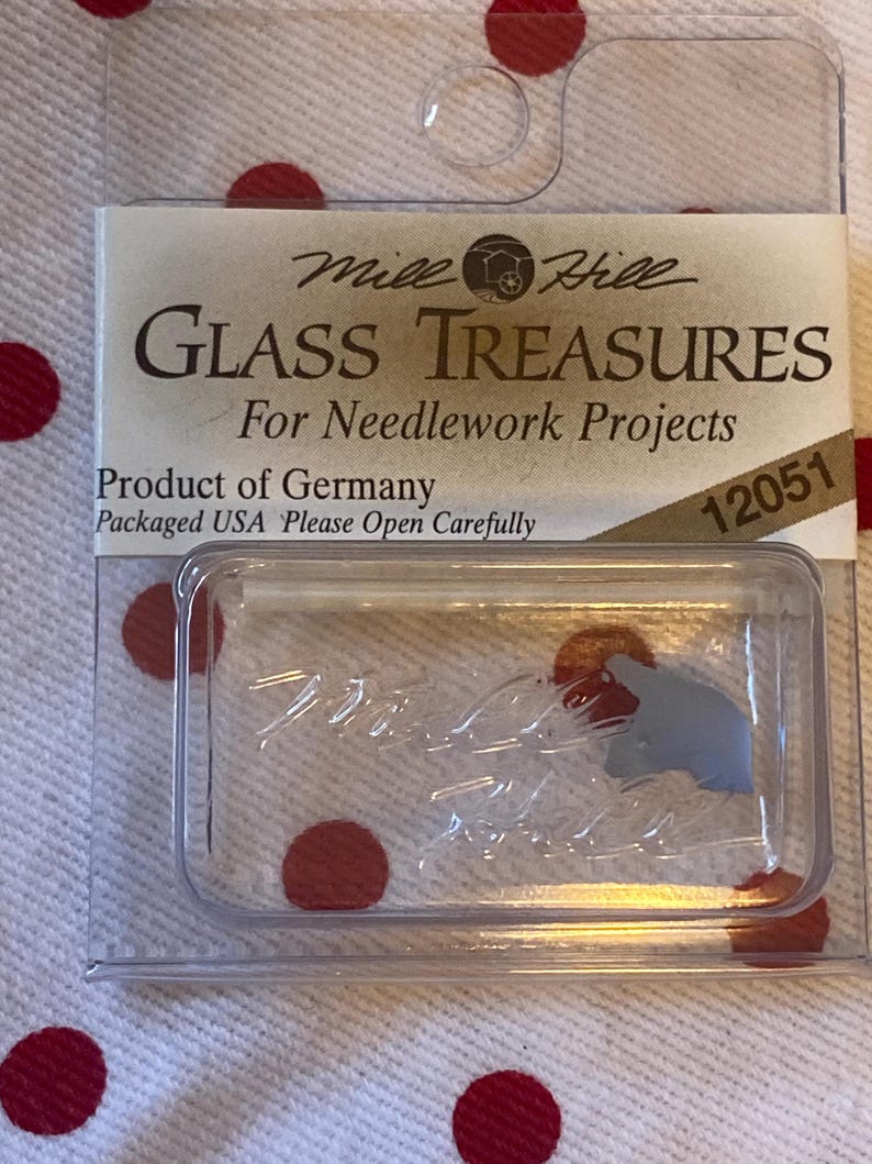 May include: A clear plastic container with a small piece of gray glass inside. The container has a label that reads "Mile Hill Glass Treasures For Needlework Projects Product of Germany Packaged USA Please Open Carefully 12051".