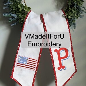 May include: White banner with red star trim and a red, white, and blue embroidered American flag and the letter "P". The banner has the text "VMadeltForU Embroidery". The banner is hanging on a green wreath.