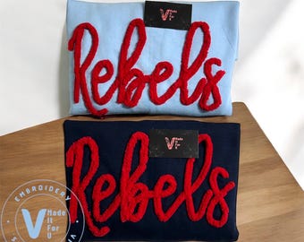 May include: Two t-shirts with the word "rebels" embroidered in red on the front. The shirts are blue and navy blue.