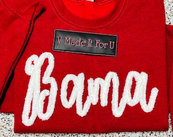 May include: Red sweatshirt with the word "Bama" in white, fluffy lettering. A black rectangular patch at the top reads "V Made It For U" in pink lettering. The sweatshirt is a crew neck style.
