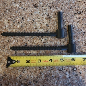 Könnte beinhalten: Zwei schwarze Türscharniere mit Schrauben liegen neben einem gelben Maßband. Das Band zeigt zwischen 5 und 18 cm an. Die Scharniere sind aus Metall und für Tore oder Türen bestimmt.