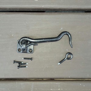 May include: Black metal hook and eye latch with four screws. The hook is curved and the eye is round. The latch is designed for doors or gates.
