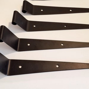 May include: Four black metal hinges with rounded ends and multiple holes. The hinges are arranged in a row, with the top hinge at the top of the image and the bottom hinge at the bottom of the image.