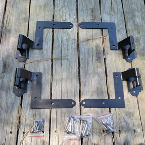 May include: Four black metal hinges with decorative accents, laid out on a wooden surface.  The hinges are accompanied by four bags of screws.