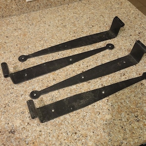 Puede incluir: Cuatro bisagras de metal negro con extremos redondeados. Las bisagras son todas del mismo tamaño y forma, y están dispuestas en una fila.