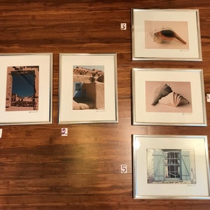 May include: Five framed photographs with silver frames. The photos are of a blue door, a seashell, a window, a seashell, and a view through a window.