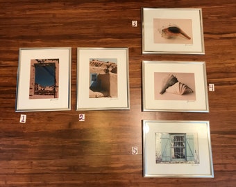 May include: Five framed photographs with silver frames. The photos are of a blue door, a seashell, a window, a seashell, and a view through a window.