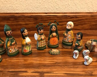 May include: A set of hand-painted wooden nativity figurines featuring various characters including figures in green, yellow, and orange robes, an angel, a central infant in a manger, and several small animal figures with floral details.