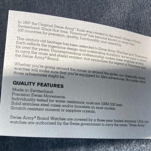 May include: A white paper with text about Swiss Army watches. The text highlights quality features such as Swiss-made, precision movements, water resistance to 100M (330 feet), stainless steel cases, and scratch-resistant crystals. The text also mentions a three-year limited warranty.