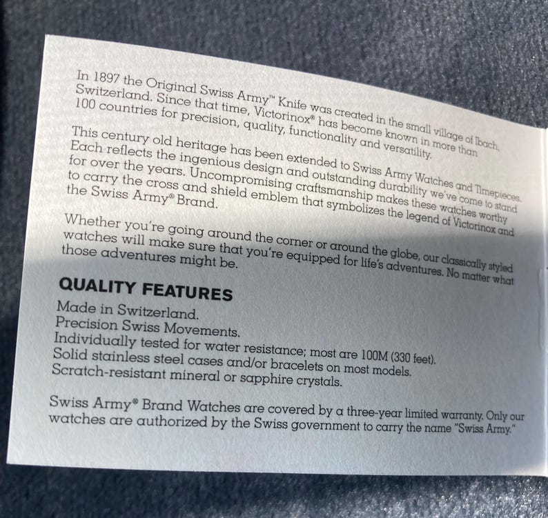 May include: A white paper with text about Swiss Army watches. The text highlights quality features such as Swiss-made, precision movements, water resistance to 100M (330 feet), stainless steel cases, and scratch-resistant crystals. The text also mentions a three-year limited warranty.