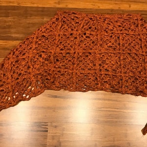 May include: A crocheted shawl in a burnt orange color with a lacy pattern.
