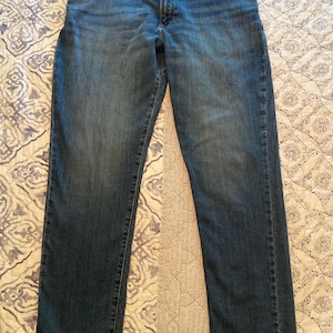 May include: A pair of medium-wash blue denim jeans with a straight-leg cut. The jeans feature a Lee brand label on the interior waistband, a metal button closure, a zipper fly, five pockets, and visible stitching along the seams and hems.