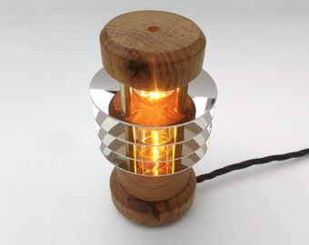 Puede incluir: Una lámpara de mesa de madera con una pantalla cromada y una bombilla de luz blanca cálida. La lámpara tiene una base redonda y una pantalla cilíndrica con múltiples capas de cromo.