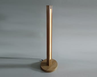 May include: A wooden floor lamp with a rectangular base and a tall, slender column. The column has a thin, vertical slit that emits a warm, white light.