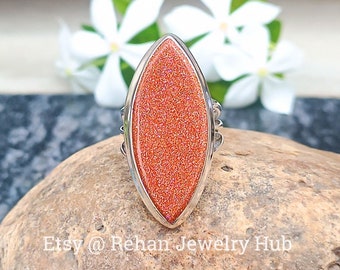 May include: A silver ring with a large, oval-shaped, orange sunstone. The stone is sparkly and has a marbled pattern.