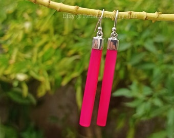May include: A pair of pink dangle earrings with silver hooks and silver caps on the ends of the pink rods. Etsy @ Rehan Jewelry Hub is printed on the background.