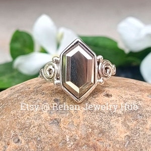 Pode incluir: Um anel de prata com uma pedra preciosa hexagonal. O anel tem um design decorativo na banda.