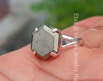 Puede incluir: Un anillo de plata con una piedra preciosa de pirita hexagonal. El anillo se lleva en un dedo.