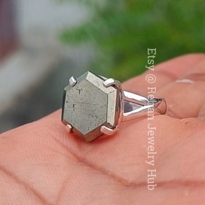 Pode incluir: Um anel de prata com uma pedra preciosa de pirita hexagonal. O anel é usado em um dedo.