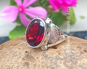 Puede incluir: Un anillo de plata con una gran piedra roja de forma ovalada. El anillo tiene intrincados diseños florales en la banda.