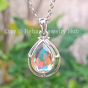 Op de afbeelding: Een zilverkleurige hangerketting met een peervormige, iriserende edelsteen. De edelsteen toont een spectrum aan kleuren, waaronder oranje, blauw en groen. De hanger hangt aan een fijne ketting. De tekst "Etsy @ RehaJewelry Hub" is zichtbaar.