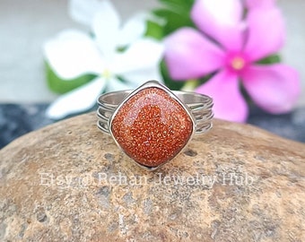 May include: A silver ring with a square-shaped, orange sunstone gemstone. The ring has a simple, elegant design.