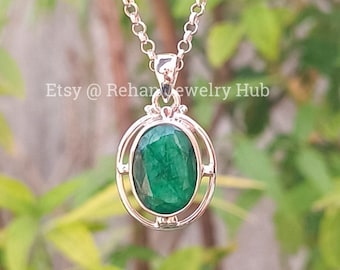 May include: A silver pendant necklace with a green oval emerald gemstone set in a silver frame. The pendant is on a silver chain.
