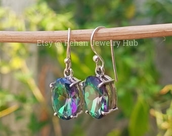 May include: Silver dangle earrings with oval-shaped iridescent gemstones. The gemstones have a rainbow of colors, including green, blue, purple, and red.