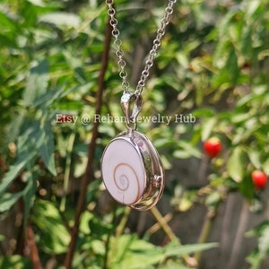May include: A silver chain necklace with a pendant featuring a white seashell with a brown spiral. The pendant is oval shaped and has a silver frame.