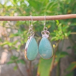May include: A pair of silver teardrop earrings with light blue gemstones. The earrings have a delicate floral design at the top.