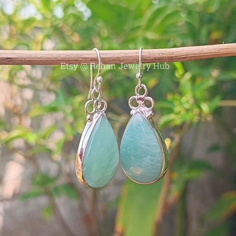 May include: A pair of silver teardrop earrings with light blue gemstones. The earrings have a delicate floral design at the top.