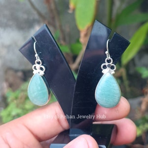 May include: A pair of silver dangle earrings with teardrop-shaped green gemstones. The earrings have a delicate floral design at the top.