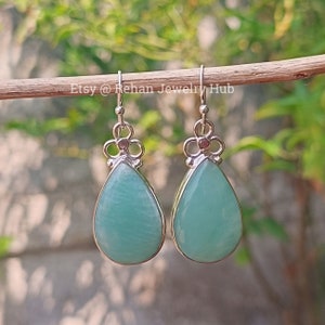 May include: A pair of silver teardrop earrings with light blue gemstone drops. The earrings have a floral design at the top.