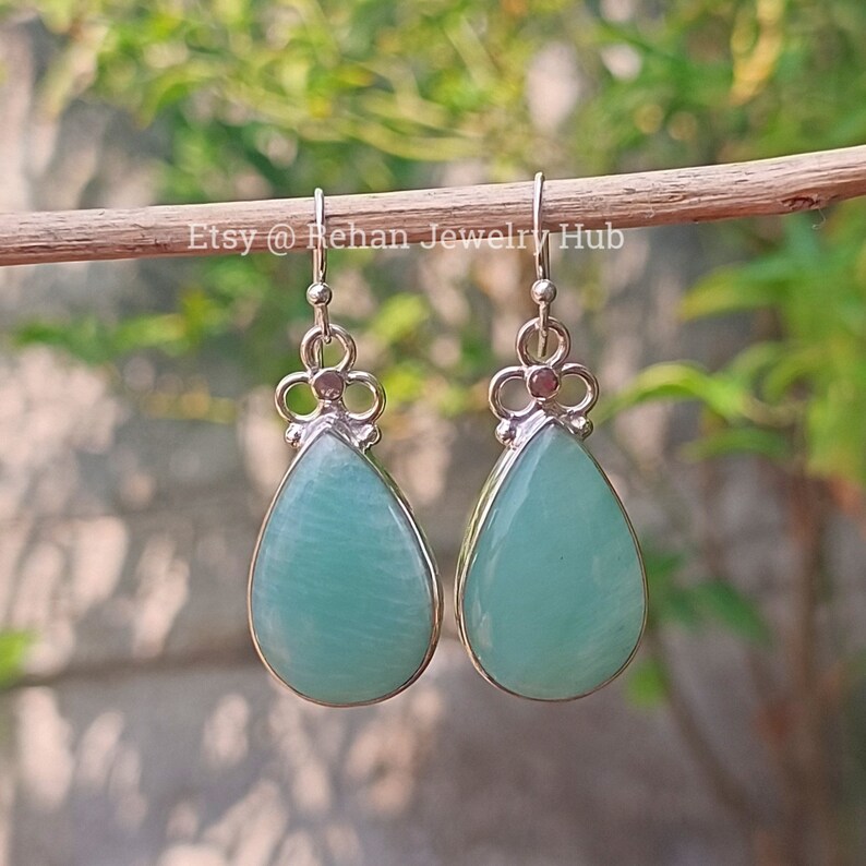 May include: A pair of silver teardrop earrings with light blue gemstone drops. The earrings have a floral design at the top.