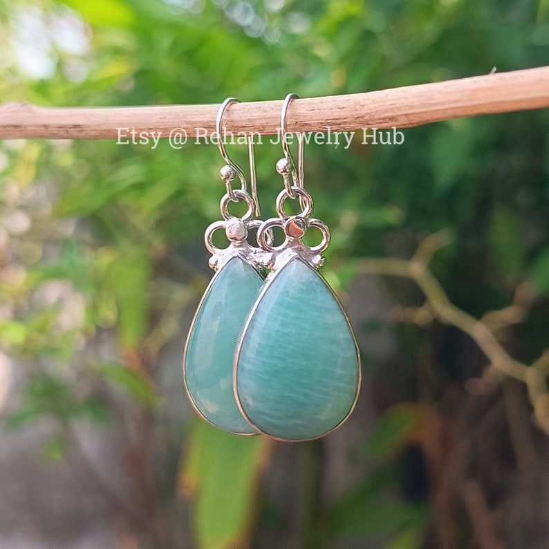 May include: A pair of silver teardrop earrings with light green gemstone drops. The earrings have a delicate floral design at the top of the drop.