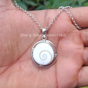 May include: A silver chain necklace with a pendant featuring a white and brown shell with a spiral pattern. The pendant is set in a silver frame with a circular design. The text "Etsy @ Rehan Jewelry Hub" is visible in the image.