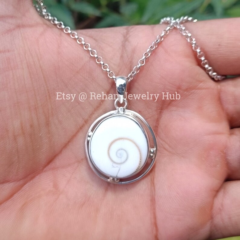 May include: A silver chain necklace with a pendant featuring a white and brown shell with a spiral pattern. The pendant is set in a silver frame with a circular design. The text "Etsy @ Rehan Jewelry Hub" is visible in the image.
