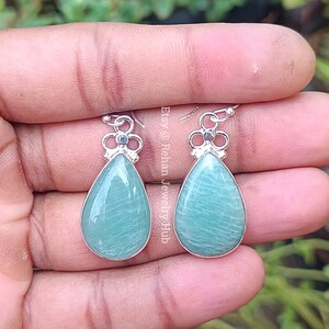 May include: A pair of silver dangle earrings with light green teardrop-shaped gemstones. The earrings have a delicate floral design at the top.