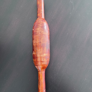 May include: A wooden rolling pin with a brown finish. The rolling pin is approximately 30 cm long and has a slightly rounded shape.