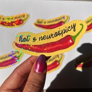 Peut inclure: Plusieurs autocollants représentant un piment rouge avec l'inscription "hot & neurospicy" en noir. Les autocollants ont un fond jaune et un effet pailleté holographique.