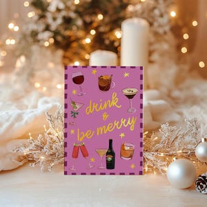 May include: A greeting card with a purple background and the words "drink & be merry" in gold script. The card features illustrations of various cocktails and a bottle of liquor. The background includes Christmas decorations and lights.