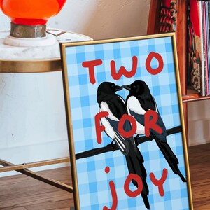 May include: A framed print with a blue and white checkered background. Two black and white magpies are perched on a branch. The text "TWO FOR JOY" is written in red letters.